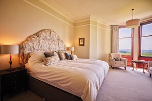 A large bed with a patterned headboard, a nightstand with a lamp, a chair, a table, and a view of the outdoors through a window. - Kinclune House & Annex Luxury Mansion, Angus Glens (Kirkton of Kingoldrum)