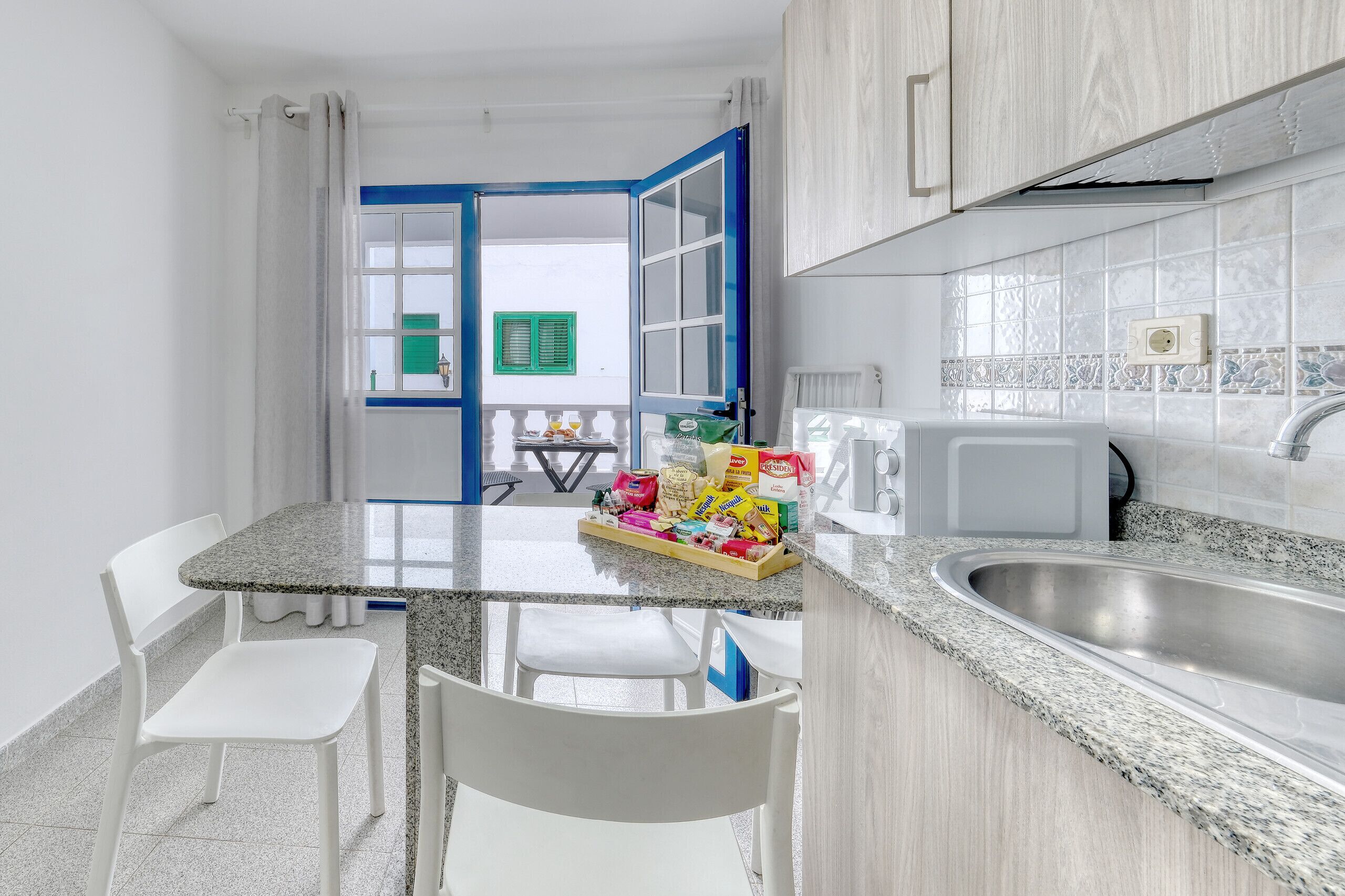 Une cuisine de taille réduite, dotée d’un plan de travail en granit, de chaises blanches et d’une table à manger.