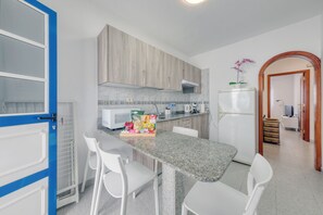 Une cuisine de taille réduite, dotée d’un plan de travail en granit, de chaises blanches et d’un four à micro-ondes.
