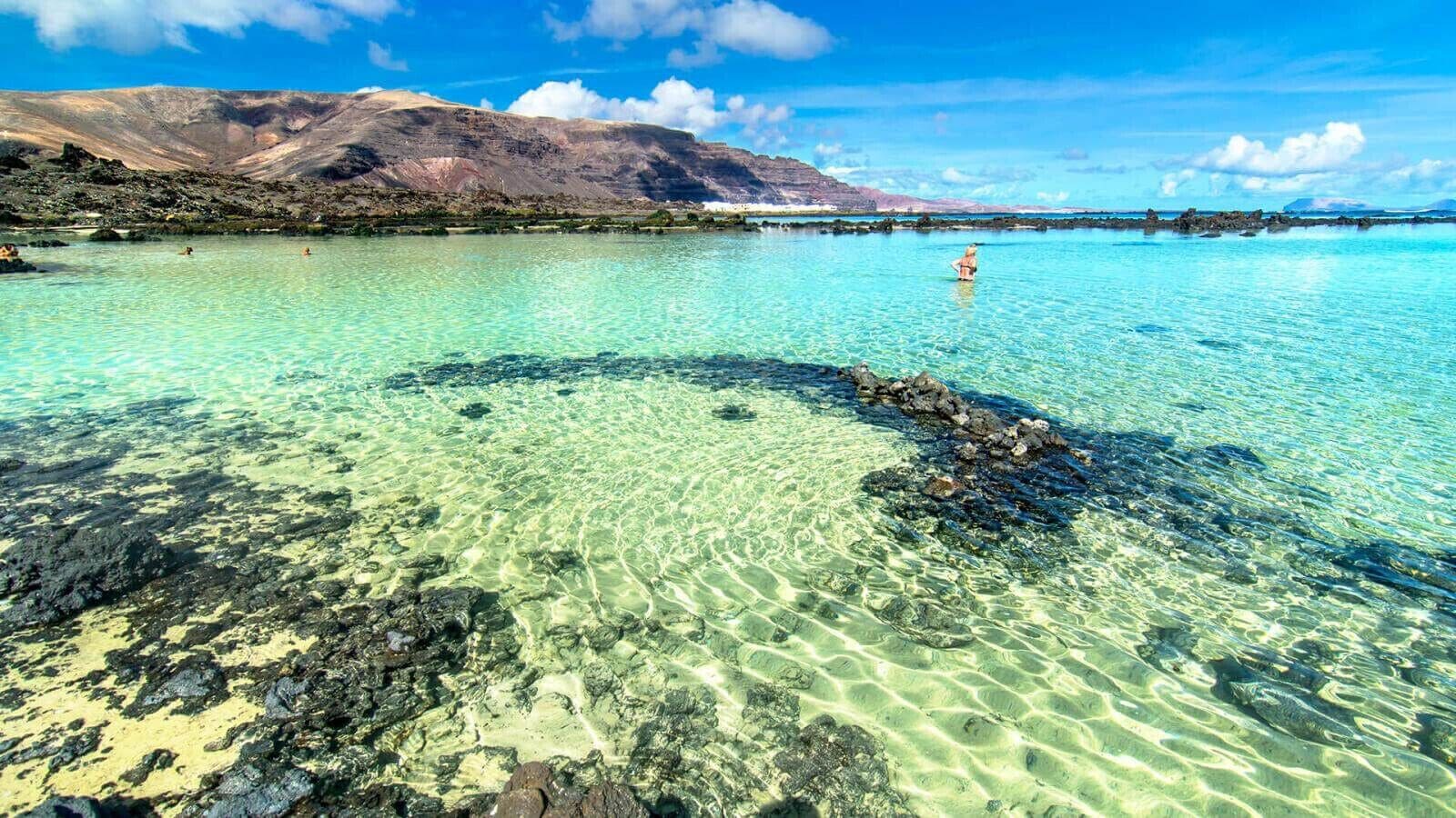 Helder turquoise water met rotsformaties en een bergketen in de verte.