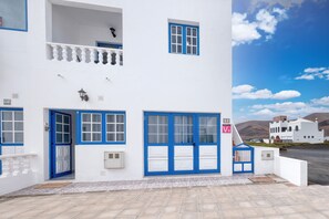 Un bâtiment blanc avec des portes et des fenêtres bleues, un balcon et un ciel dégagé.