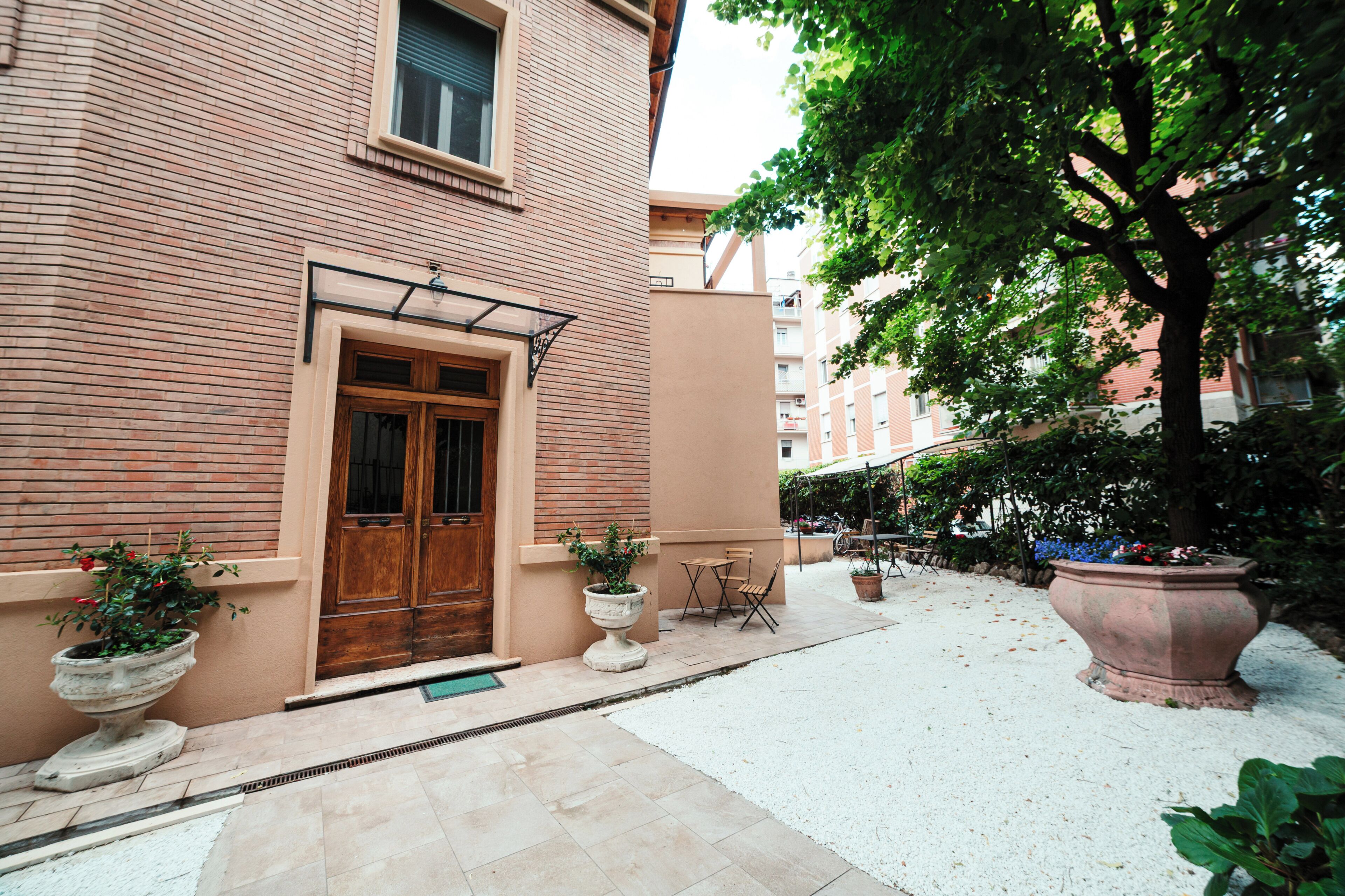 A courtyard with a brick building, a wooden door, potted plants, and outdoor seating.