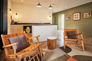 A modern kitchen with white cabinets, a black countertop, and a wooden dining table with chairs. There are two pendant lights above the table. - Stylish Barn Conversion, Woodland Views, Angus (Kirkton of Kingoldrum)