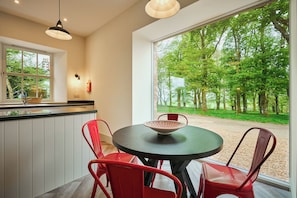 A modern kitchen with a round dining table, red chairs, and a large window with a view of a forest. - Stylish Barn Conversion, Woodland Views, Angus (Kirkton of Kingoldrum)