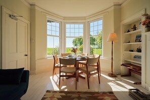 Un coin repas avec une table dressée pour quatre personnes, de grandes fenêtres et une bibliothèque agrémentée d’objets décoratifs.