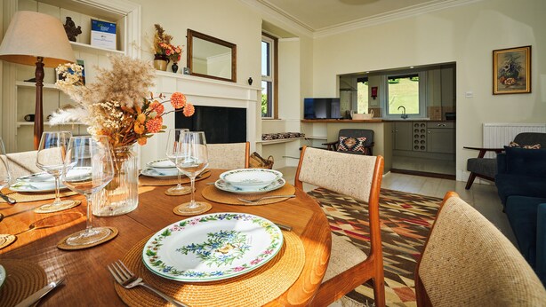 A dining room with a wooden table set for four, surrounded by wicker chairs. A fireplace with a mirror above it is visible in the background. - Peaceful Farmhouse, Kinclune Estate, Angus Glens (Kirkton of Kingoldrum)