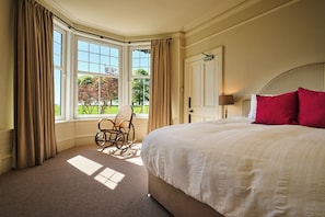 A bedroom with a large bed, a chair by the window, and a view of the outdoors. - Peaceful Farmhouse, Kinclune Estate, Angus Glens (Kirkton of Kingoldrum)