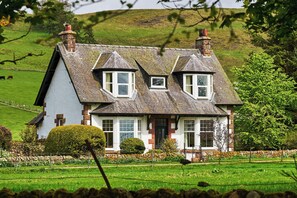 Une maison à deux étages, dotée d’un toit à forte pente, de lucarnes et d’une cheminée en pierre.