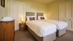 A hotel room with two beds, a wooden dresser, a nightstand with a lamp, and a framed picture on the wall. - Peaceful Farmhouse, Kinclune Estate, Angus Glens (Kirkton of Kingoldrum)