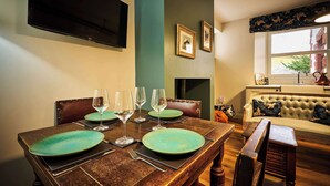 A dining room with a wooden table set for four, a television mounted on the wall, and a sofa in the background. - Osprey Annex family suite at Kinclune Estate, Angus (Kirkton of Kingoldrum)