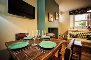 A dining room with a wooden table set for four, a television mounted on the wall, and a sofa in the background. - Osprey Annex family suite at Kinclune Estate, Angus (Kirkton of Kingoldrum)