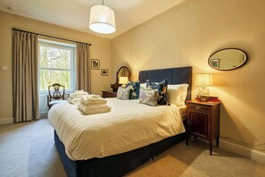A neatly made bed with pillows, a bedside table with a lamp, and a window with curtains. - Osprey Annex family suite at Kinclune Estate, Angus (Kirkton of Kingoldrum)