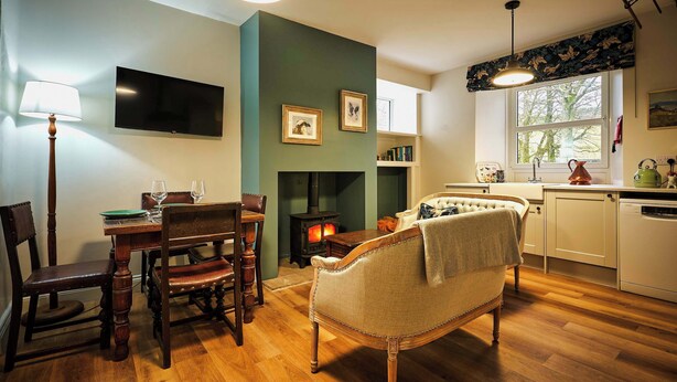 A cozy living room with a fireplace, wooden furniture, a television, and a dining area with chairs and a table. - Osprey Annex family suite at Kinclune Estate, Angus (Kirkton of Kingoldrum)