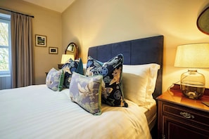 Une chambre d’hôtel avec un lit, des oreillers, une table de chevet, une lampe et une fenêtre avec des rideaux.