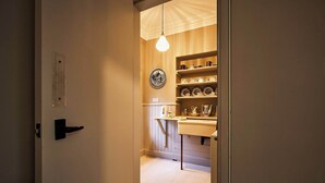 A narrow hallway leading to a kitchen area with shelves of dishes and a hanging light bulb. - Osprey Annex family suite at Kinclune Estate, Angus (Kirkton of Kingoldrum)