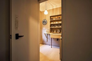 A narrow hallway leading to a kitchen area with shelves of dishes and a hanging light bulb. - Osprey Annex family suite at Kinclune Estate, Angus (Kirkton of Kingoldrum)