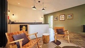 Une cuisine moderne avec des armoires blanches, un comptoir noir et un îlot central intégré. On y trouve deux chaises en bois avec des coussins, un tabouret rond en bois et un tapis à motifs sur le sol.