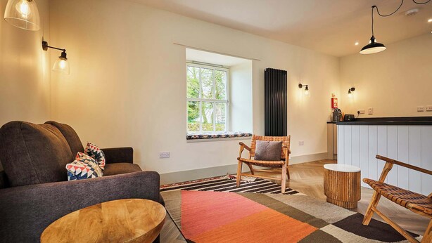 Un salon comprenant un canapé, un fauteuil, une table d’appoint en bois et un tapis à motifs.