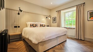 Une chambre à coucher avec un grand lit, des lampes de chevet, un banc, un radiateur et une fenêtre avec des rideaux.