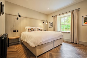 A bedroom with a large bed, bedside lamps, a bench, a radiator, and a window with curtains. - Barn Conversion at Kinclune Steading, Angus Glens (Kirkton of Kingoldrum)