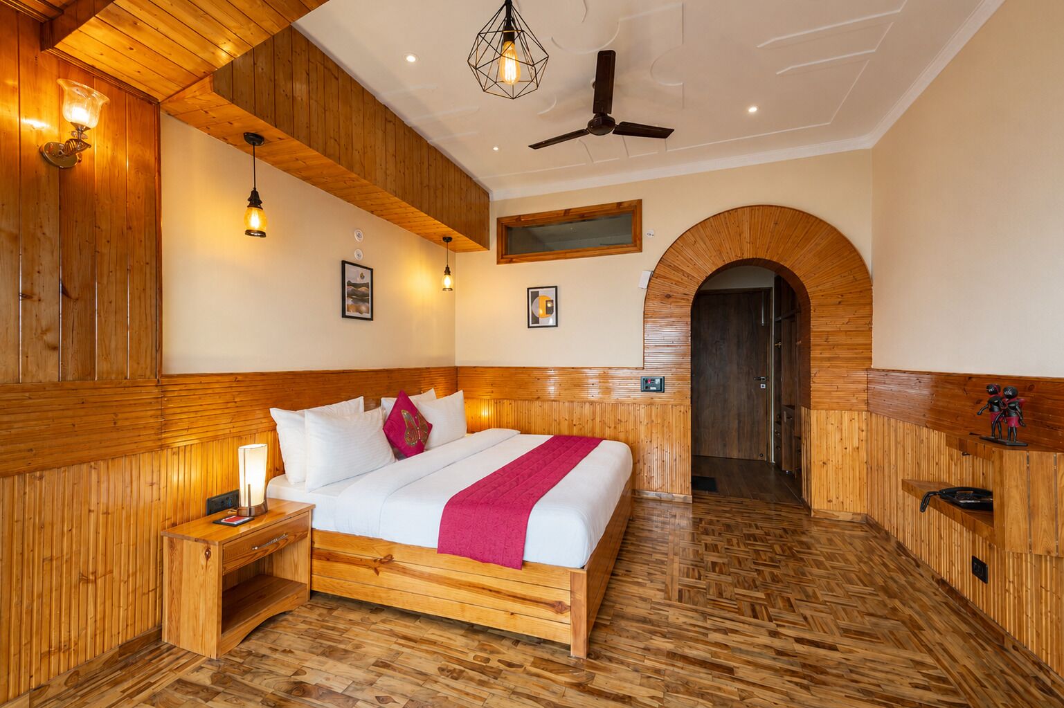 Quarto de hotel com cama de madeira, mesas de cabeceira, ventoinha no teto e piso de madeira.