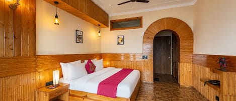 Una habitación de hotel con cama de madera, mesitas de noche, ventilador de techo y piso de madera.