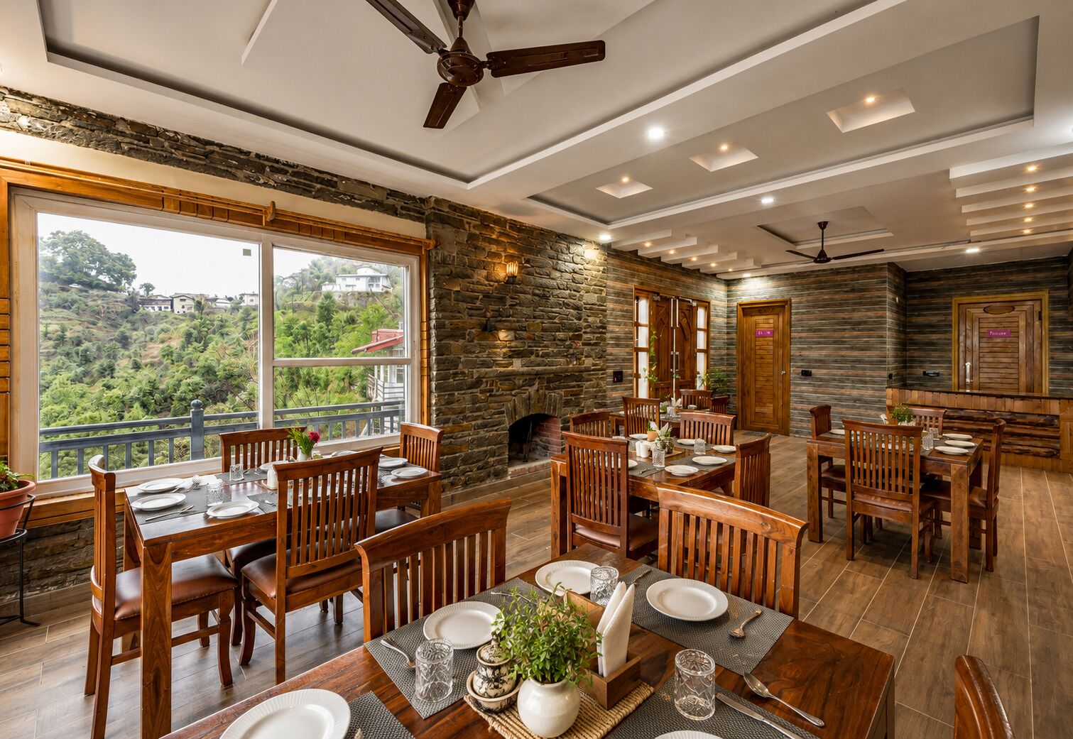 Uma sala de jantar com mobiliário de madeira, uma parede de pedra e vista para o verde.