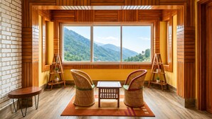 Una habitación con un ventanal grande, paredes de madera, dos sillas de mimbre, una mesita y una pared de ladrillo.