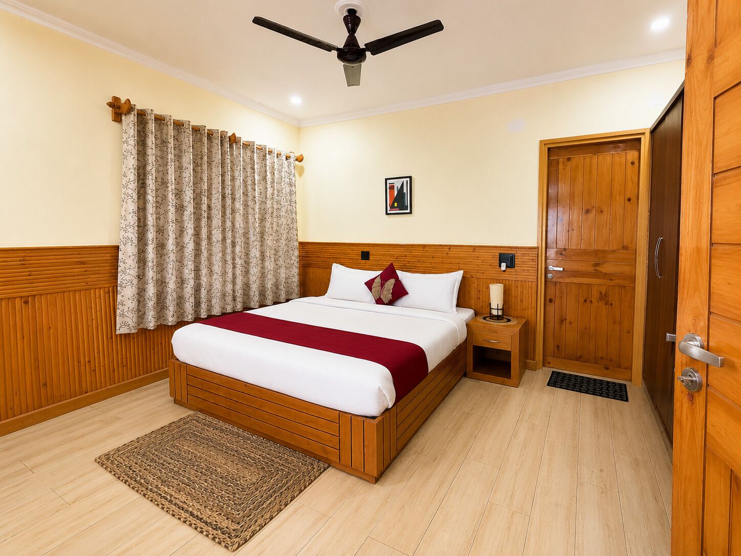 Habitación de hotel con cama de madera, mesita de noche con lámpara, ventilador de techo y armario de madera.