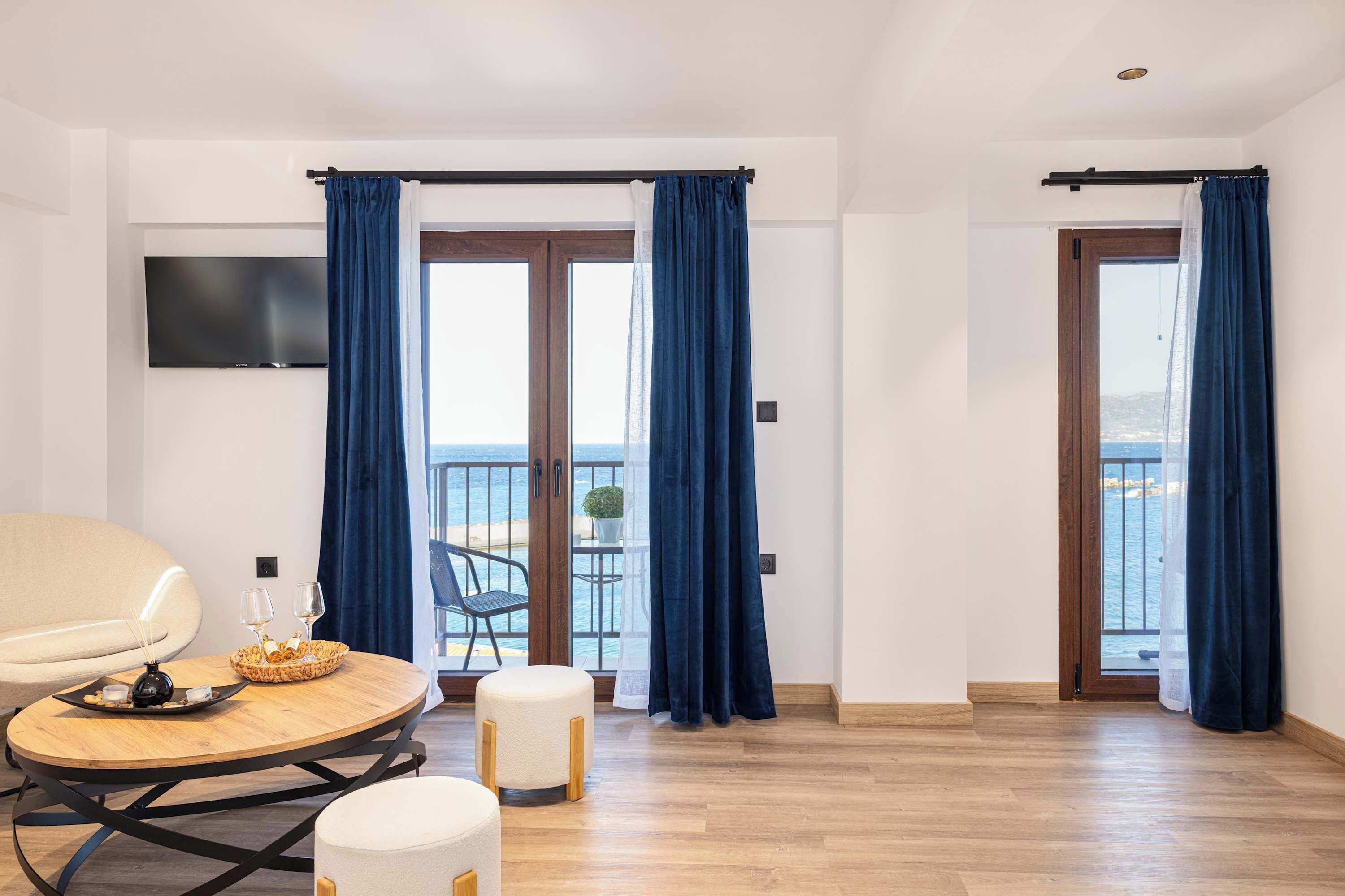 A modern room with a round wooden table, a beige chair, and a balcony with blue curtains.