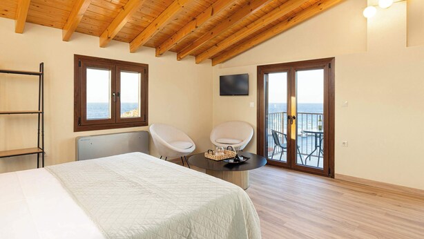 A bedroom with a bed, two chairs, a TV, and a balcony with a view. - Studio Tepes - Velis Samos Sea View Balcony Suite (Kokkari)