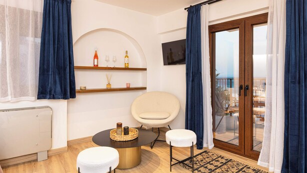 Ein modernes Wohnzimmer mit einem runden Tisch, zwei weißen Hocker, einem Fernseher und einem Balkon mit Blick.