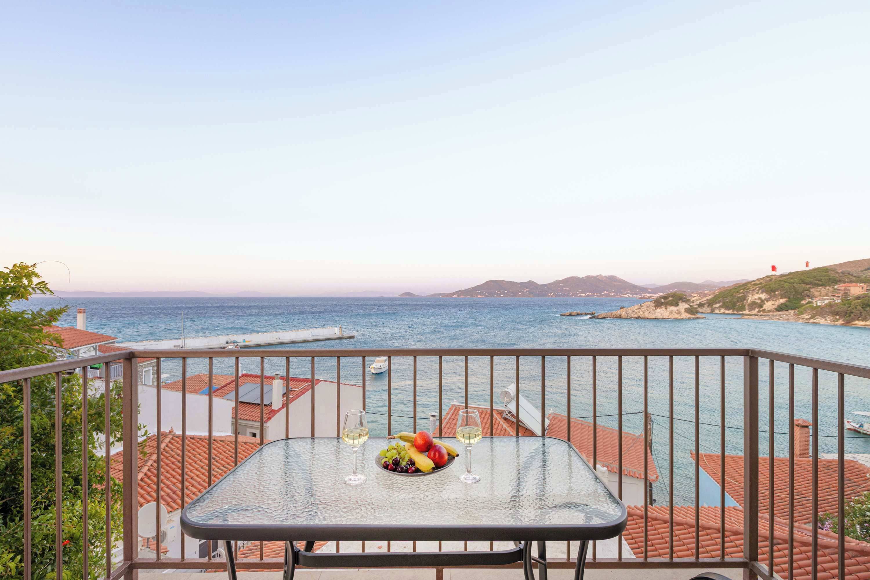 Ein Balkon mit Tisch für zwei Personen, der Blick auf die Küste mit Gebäuden und Booten bietet.