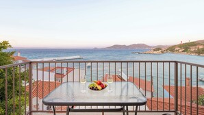 Ein Balkon mit Tisch für zwei Personen, der Blick auf die Küste mit Gebäuden und Booten bietet.