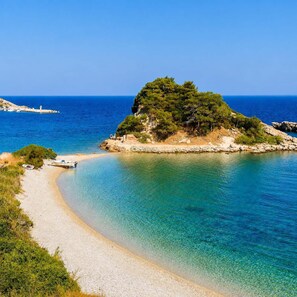 Eine Küstenlandschaft mit blauem Meer, einem Sandstrand und einer kleinen Insel mit dichter Vegetation.