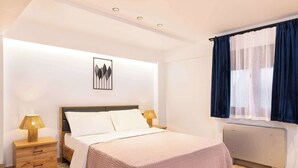 Ein Schlafzimmer mit einem Bett, Nachttischen, einem Heizkörper, einem Fenster mit Vorhängen und einem Wandbild.