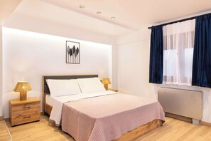 Ein Schlafzimmer mit einem Bett, Nachttischen, einem Heizkörper, einem Fenster mit Vorhängen und einem Wandbild.