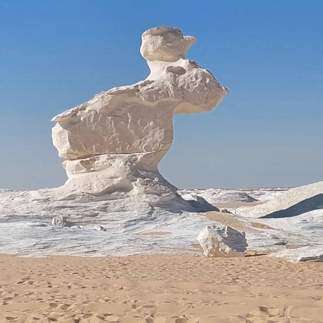 A rock formation resembling a human figure in a desert landscape.