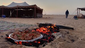 Campa de un desierto con fuego, una tienda de campaña y una persona caminando.