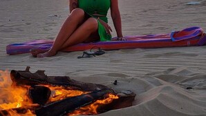Una persona sentada en la playa con una tabla de surf y un brasero cerca.