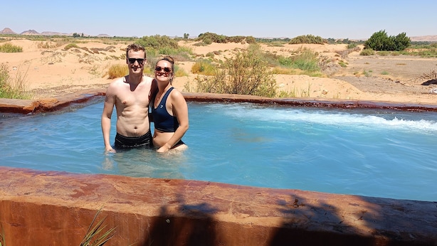 Dos personas en una piscina con un paisaje desértico al fondo.