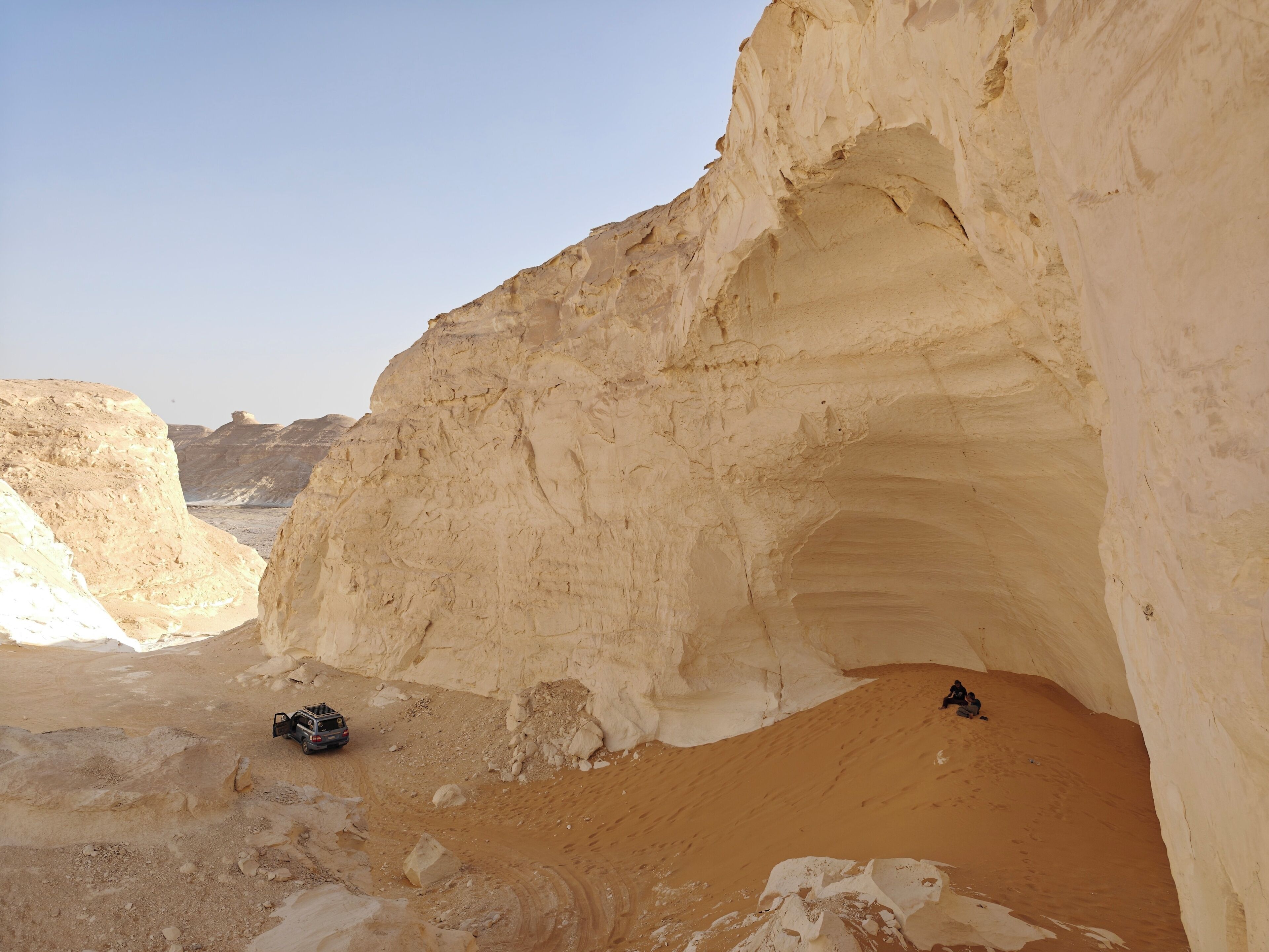 A desert landscape with a large rock formation and a vehicle.