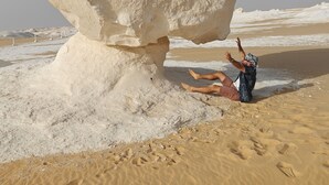 Una persona interactuando con una gran formación rocosa en una playa arenosa.