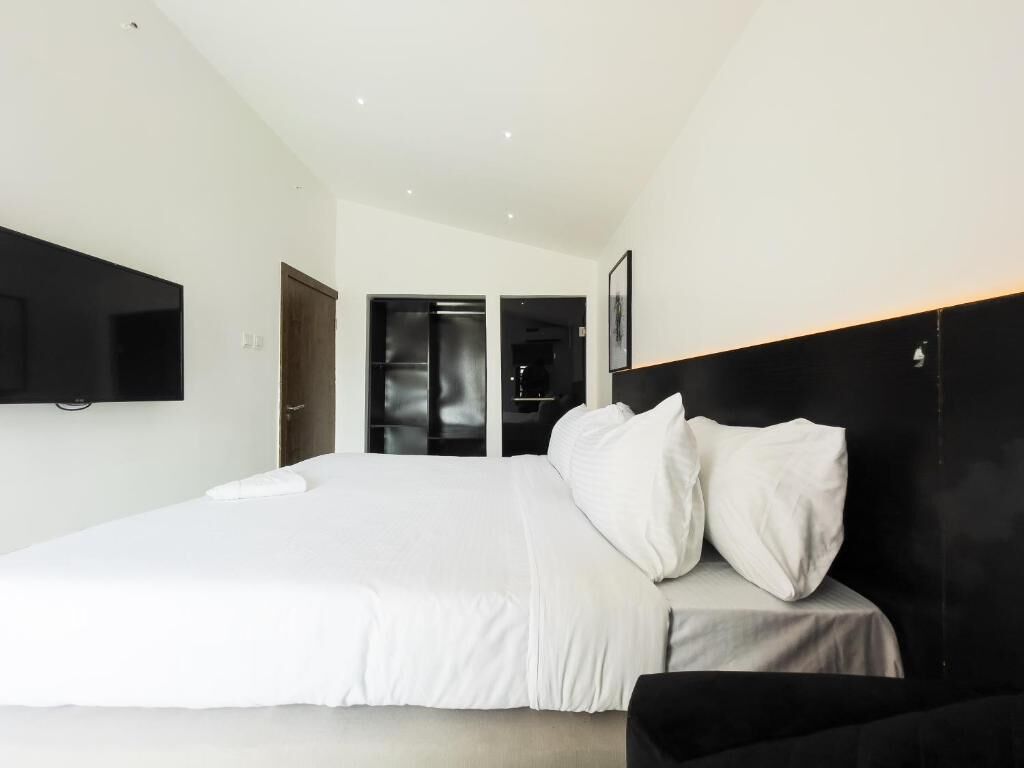 Una habitación de hotel moderna con una cama grande, un televisor de pantalla plana montado en la pared y una puerta que da a un baño.
