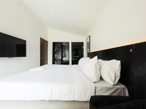 A modern hotel room with a large bed, a flat-screen TV mounted on the wall, and a door leading to a bathroom. - Yaniv Apartment (Lagos)