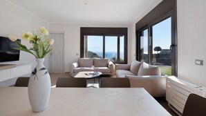 Een moderne woonkamer met een zithoek, een eettafel en een groot raam met uitzicht op zee.