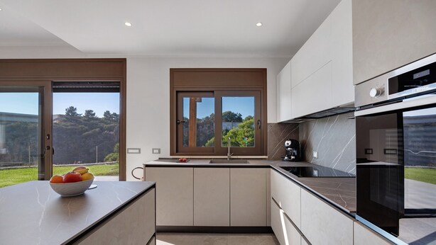 Een moderne keuken met een groot eiland, een Bosch oven en uitzicht op het buiten.