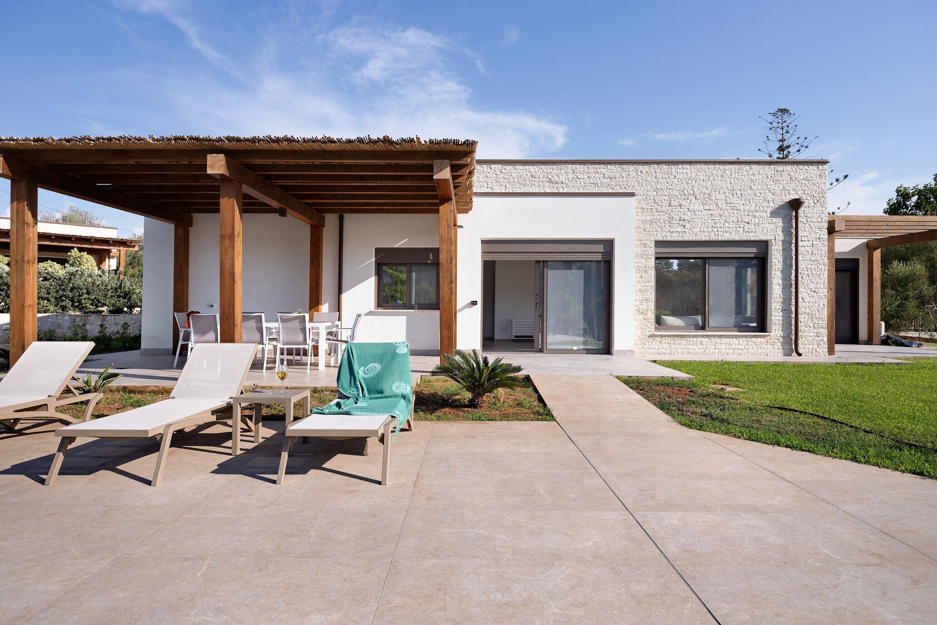 Una casa moderna con patio coperto, arredi da esterno e prato curato.