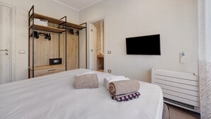 Een hotelkamer met een bed, een televisie, een kachel en een garderobe met schoenen.