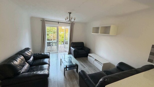 Ein modernes Wohnzimmer mit einem Glastisch, schwarzen Ledersofas und einer Schiebetür, die auf einen Balkon führt.